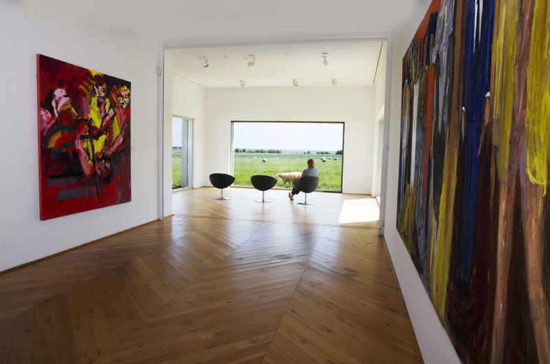 Fuglsang Kunstmuseum set indefra og ud gennem vinduet med farverig kunst på begge vægge og en person sidder og kigger ud